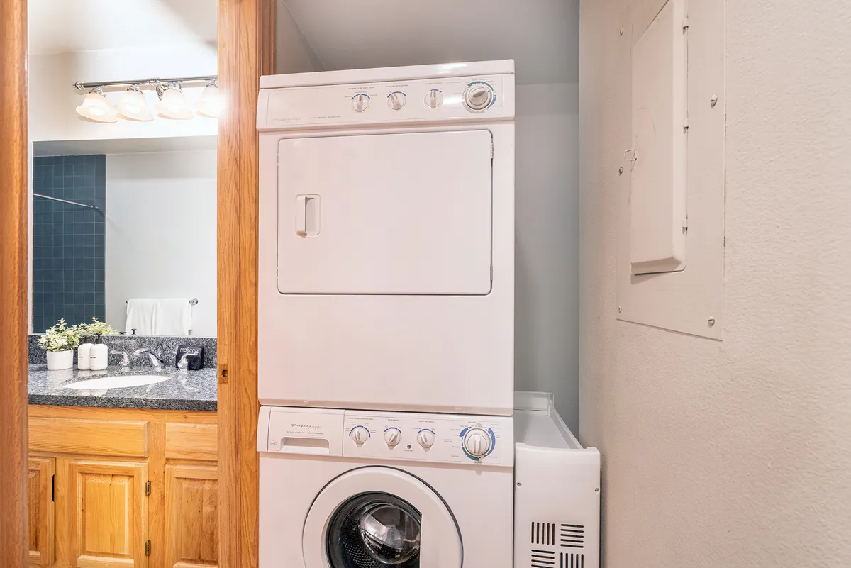 A practical interior view showing a stacked washer and dryer beside a granite countertop, with a bathroom visible in the background. It hints at the family-friendly and convenience-focused amenities available within the condo, such as laundry for families and parents.