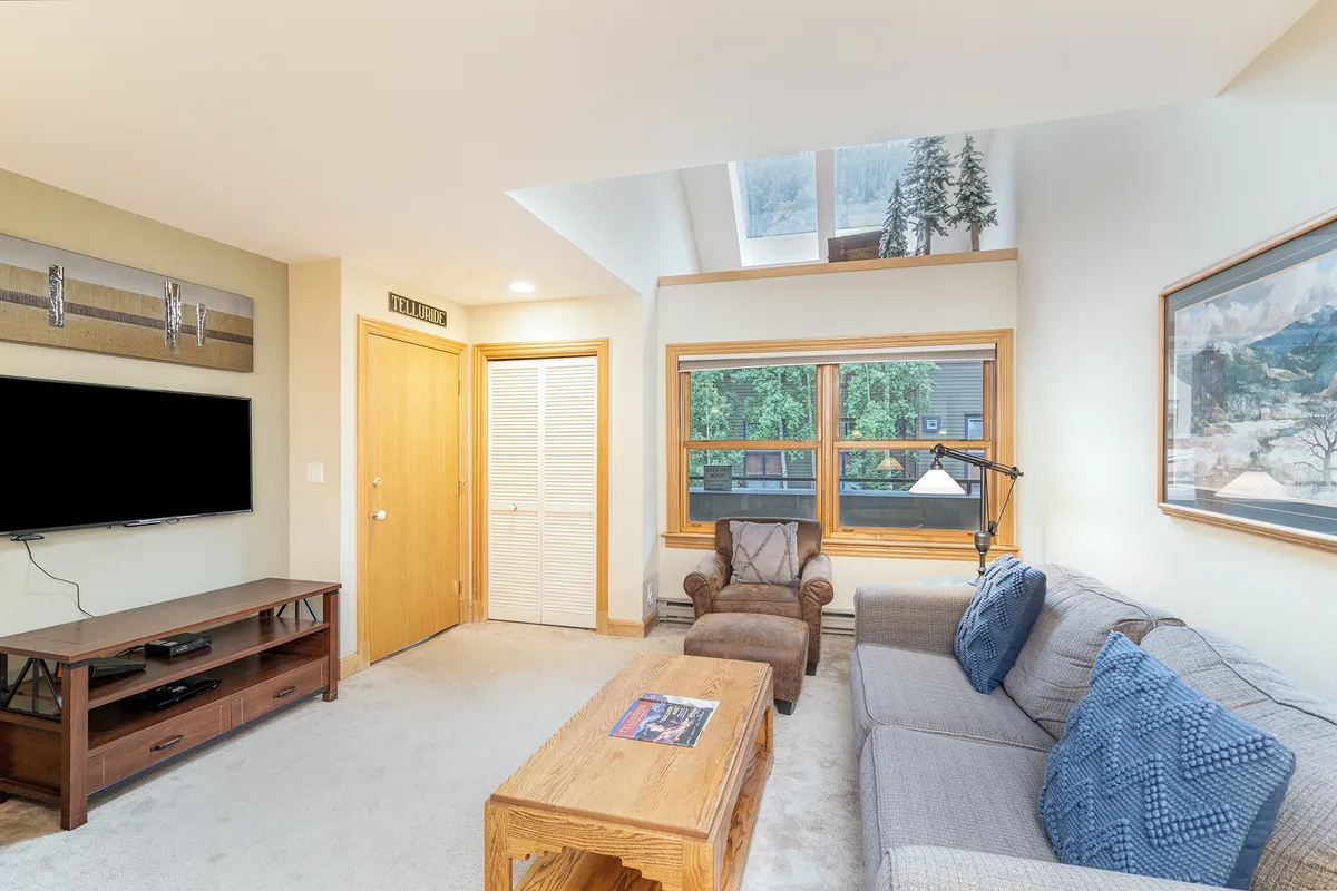 The image showcases a cozy, inviting living area with a plush sofa, stylish coffee table, and a large television, all framed by generous windows that let in plenty of natural light. The space is perfect for unwinding after outdoor adventures, hosting game nights, or gathering for a movie marathon. The decor is modern yet warm, creating a comfortable retreat for families or groups.