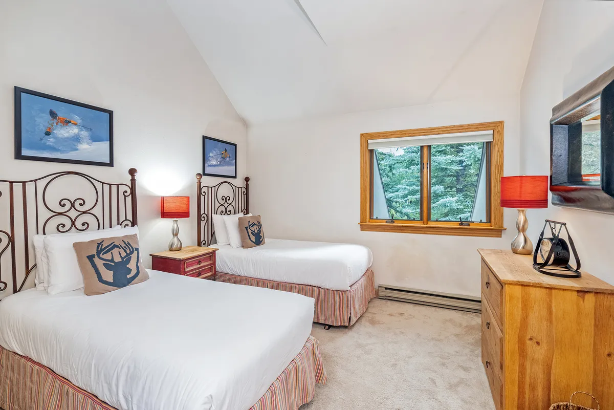 A cozy bedroom featuring inviting bed frames adorned with decorative pillows, tasteful wall art, a window that welcomes in natural light, and soft lighting from bedside lamps. There's also a dresser, creating a warm and comfortable retreat ideal for rest and relaxation.