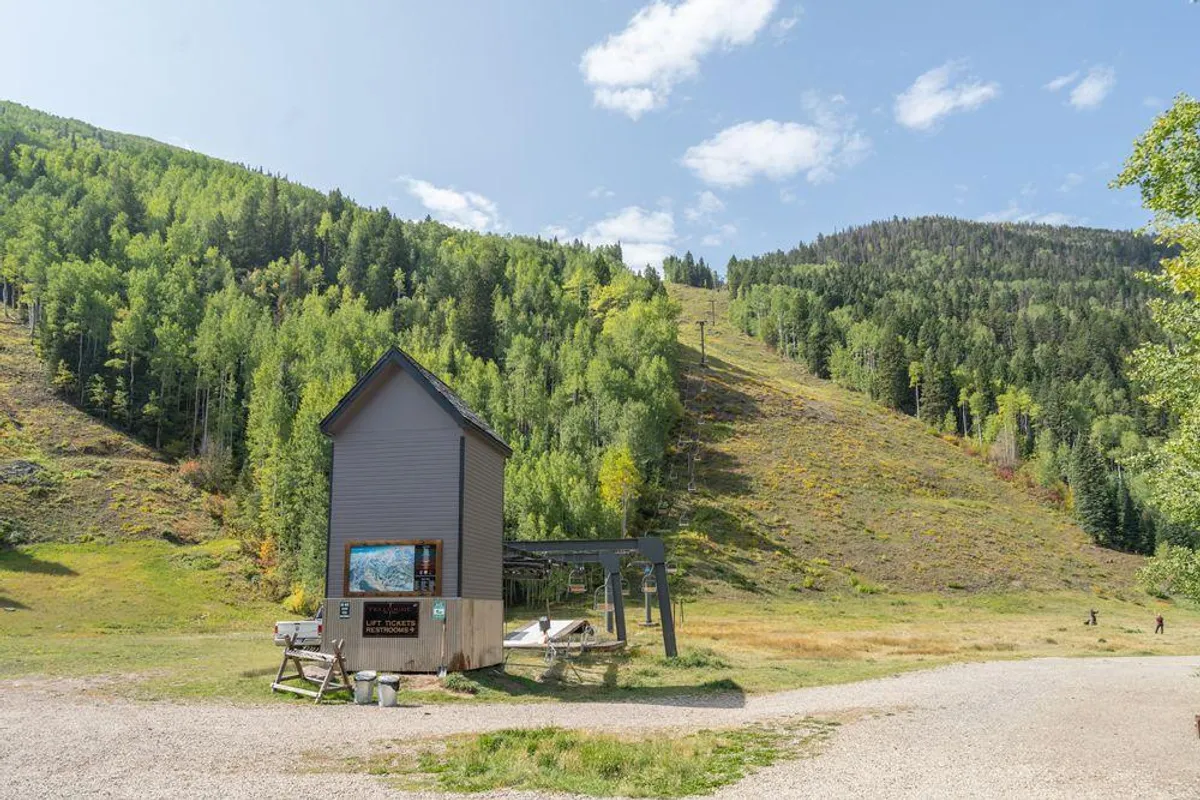A wide exterior shot capturing the building with the mountains and ski lift (Lift 7) in the background, surrounded by lush greenery. This scene situates the property within its alpine context, emphasizing the proximity to both natural vistas and ski amenities.