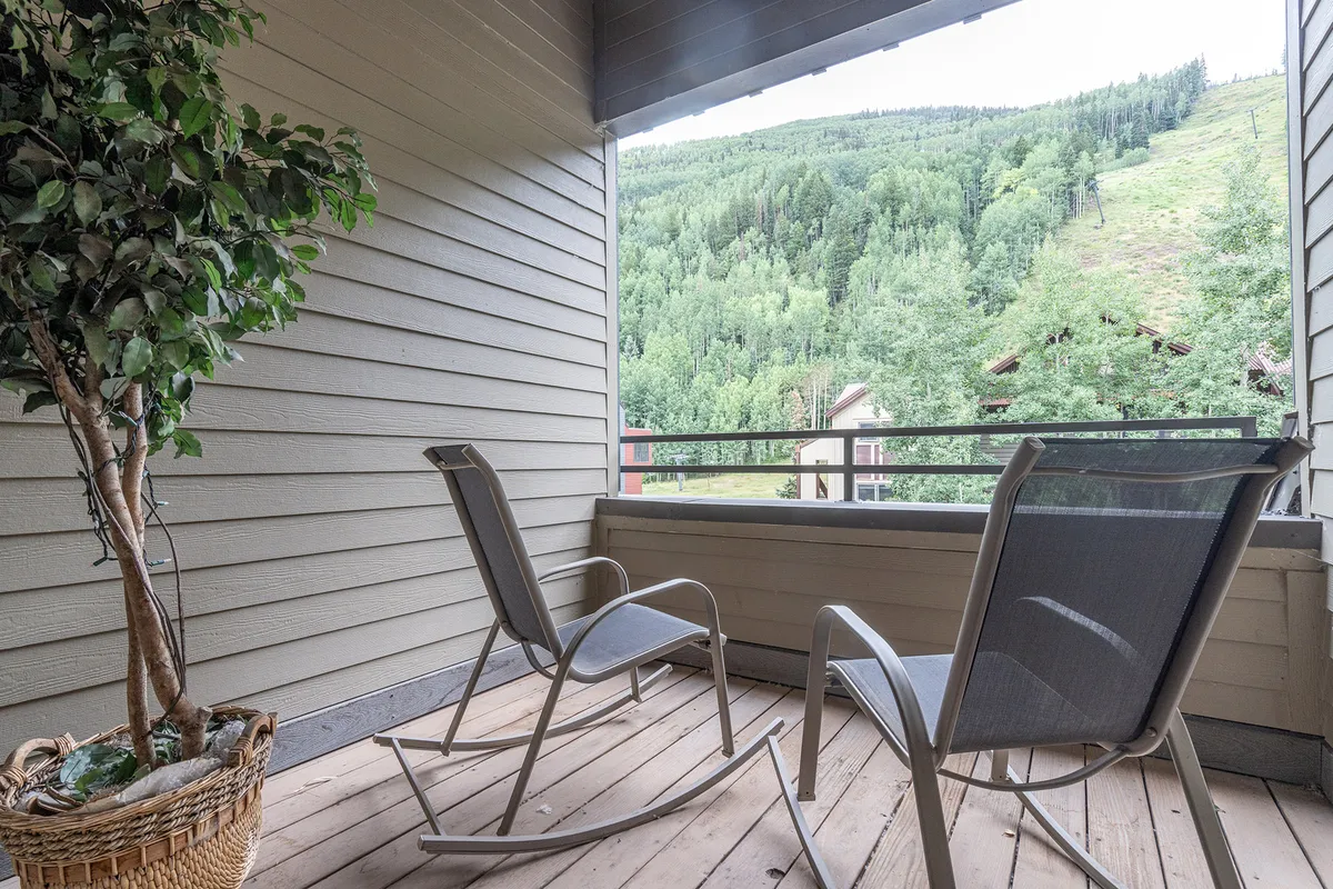 A cozy private deck featuring inviting rocking chairs and a potted plant, all oriented toward a breathtaking mountain view. The setting exudes tranquility and is perfect for relaxing, reading, or simply soaking up the natural scenery. The deck appears to offer a seamless blend of indoor comfort with an immersive outdoor experience.