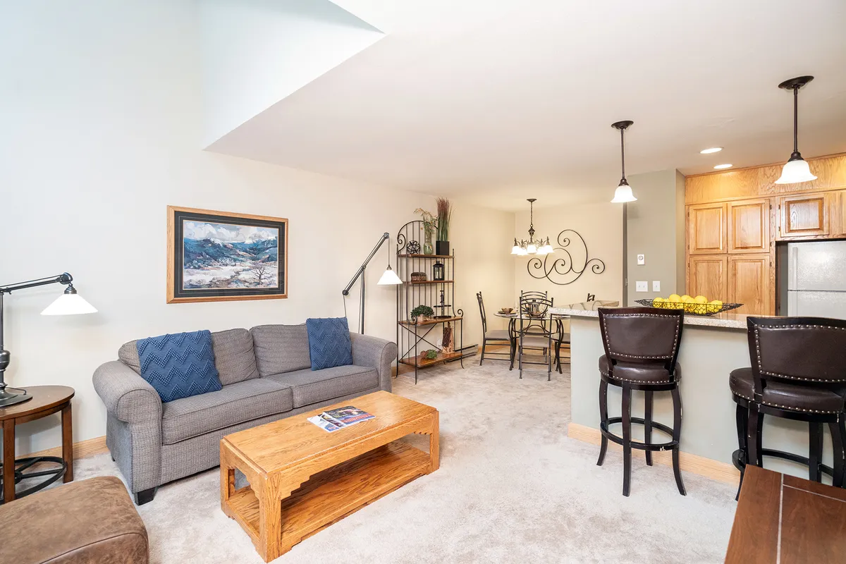 A cozy and inviting open-concept living and dining space featuring a plush sofa, a coffee table perfect for gathering around, and a dining area with a warm chandelier overhead. The arrangement encourages relaxation, conversation, and shared meals, embodying the hub-like atmosphere described in the section.