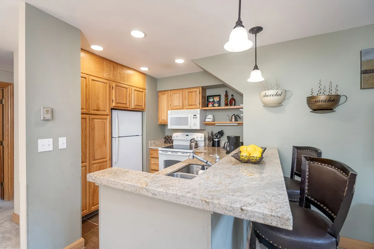 A bright, well-equipped kitchen with granite countertops, wooden cabinets, and a breakfast bar lined with comfortable bar stools. Decorative mugs add a homey touch, making the space feel ready for socializing and casual meals.